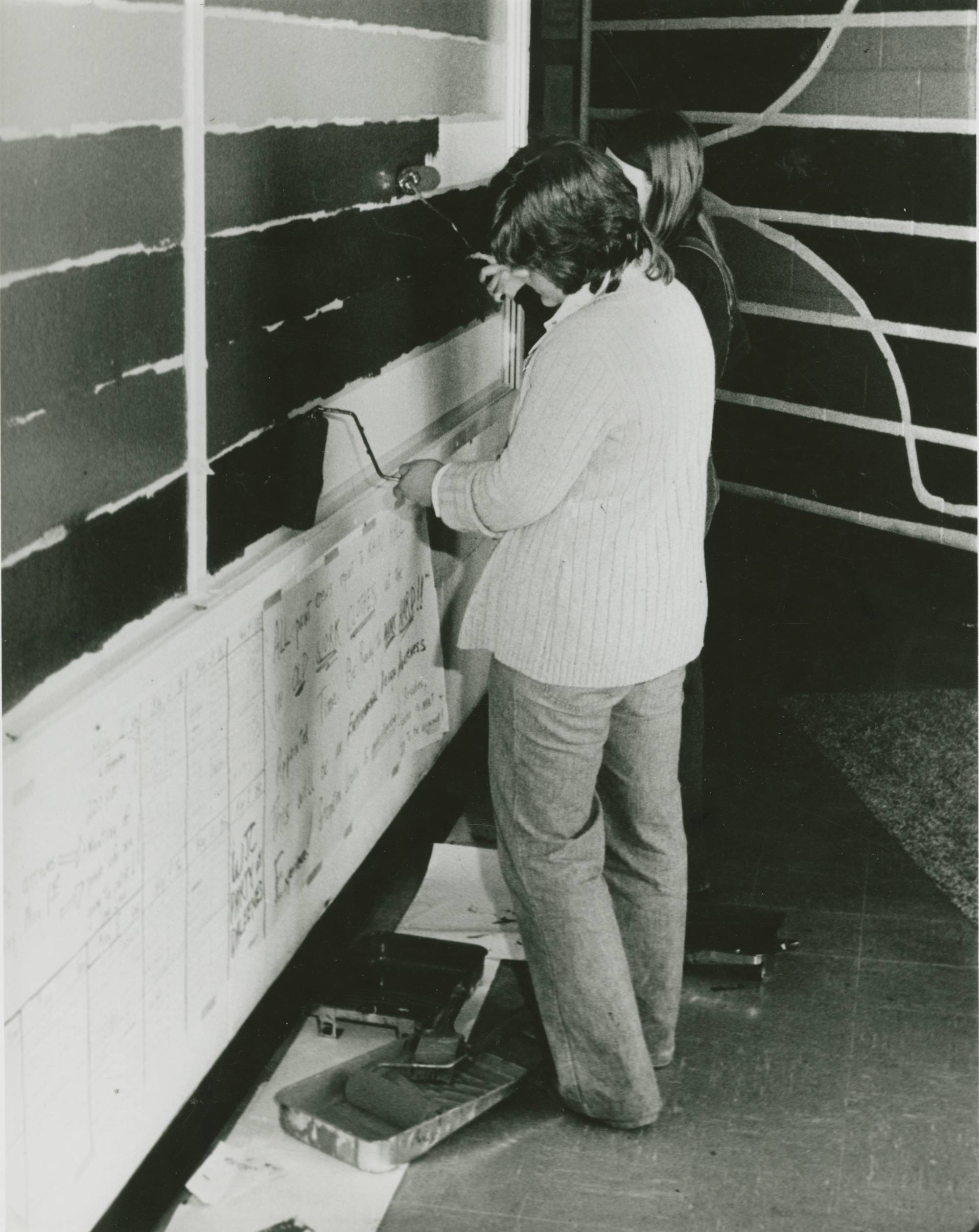A black and white photo of a student painting a mural in Lake Superior Hall.